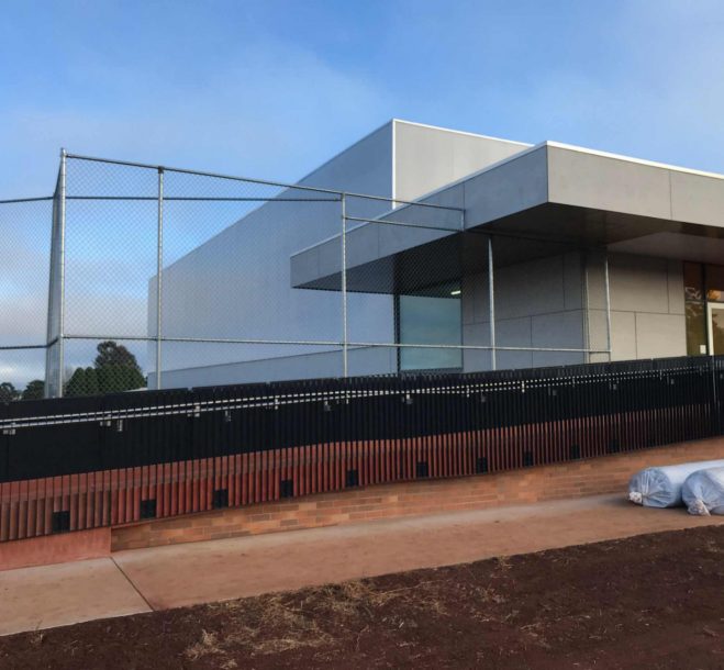 Black chainmesh security fence with rust-orange infill panels installed around a commercial building, a popular fencing Toowoomba solution for business security.